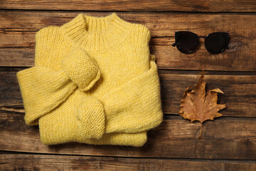 Fototapeta na wymiar Warm sweater, sunglasses and dry leaf on wooden background, flat lay. Autumn season