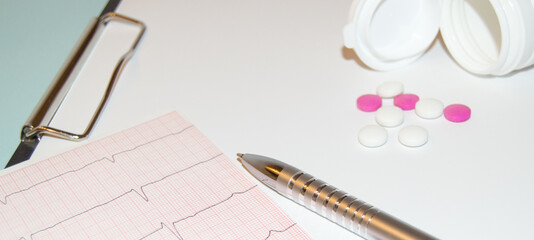 Paper cardiogram with a pen and capsules pouring out of a bottle of pills on the table, the concept of heart disease prevention