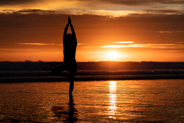 Silhouette and shadow shape of female is playing yoga on the beach during the dramatic orange sunset period. Health care and recreation action concept photo.