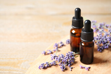 Bottles of essential oil and lavender flowers on wooden table. Space for text