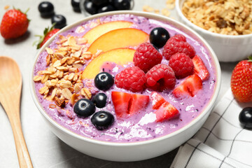 Delicious acai smoothie with fruits and oatmeal in bowl on table, closeup