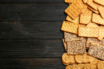 Many delicious crackers on wooden table, flat lay. Space for text