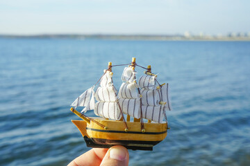 male hand holding a boat sail model, blue sea on background.