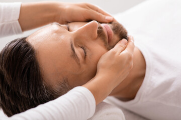 Fototapeta na wymiar Closeup of man getting healing face massage at spa