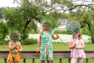 Cute little girls playing with tropical leaves outside on the deck