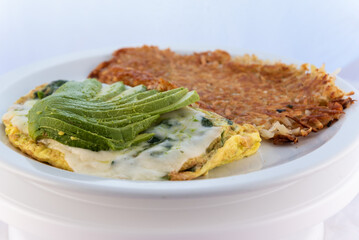 Generous serving meal of a hearty avocado omelette covered with gravy combined with hash browns.