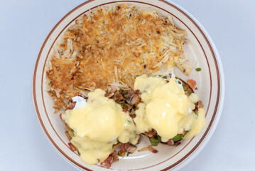 Overhead view of generous serving meal of a hearty eggs benedict stacked tall with toppings and dripping with melted cheese