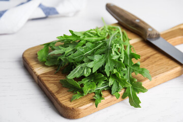 Fresh arugula, cutting board and knife on white wooden table