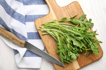 Fresh arugula, cutting board and knife on white wooden table, flat lay