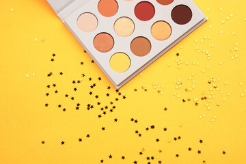 Eyeshadow palette on a yellow background and different colors of cosmetics
