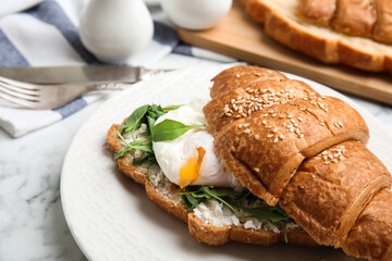 Delicious croissant with arugula and egg on white marble table, closeup