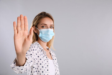 Woman in protective face mask showing stop gesture on grey background, focus on hand. Prevent spreading of coronavirus