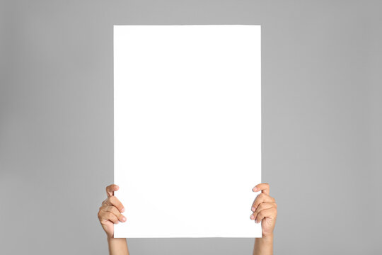 Man holding white blank poster on grey background, closeup. Mockup for design
