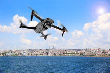 Fototapeta na wymiar Modern drone flying over sea and blurred cityscape on background. Aerial survey