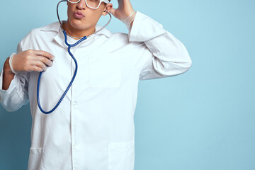 A medical worker in a dressing gown and glasses holds a stethoscope in his hands on a blue background cropped view