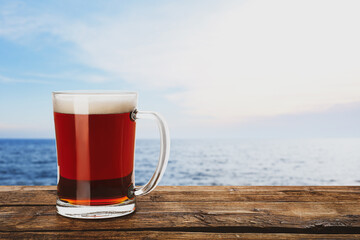 Glass mug of delicious kvass on wooden table near sea. Space for text