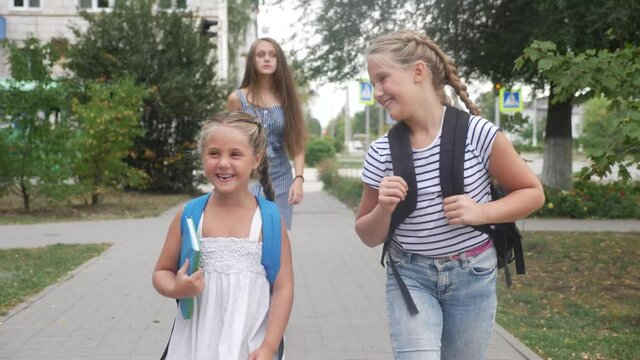 group of schoolchildren walking to school along the path. happy family school concept.little schoolgirl with backpack and textbook. schoolgirls walk along in the park to education school for lessons