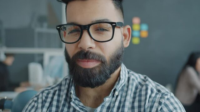 Close-up portrait of handsome Arab man wearing glasses looking at camera with serious face in office. Businesspeople, workspace and coworking concept.