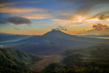 Beautiful mountain landscape during sunrise. Hills, Batur volcano and lake. Scenic panoramic view. Colorful sky with clouds. Foggy morning. Kintamani, Bali