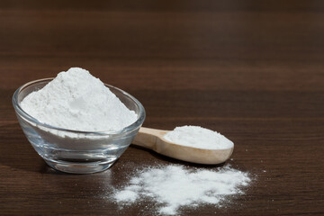 Baking soda - glass bowl and wooden spoon with baking soda; on dark wooden background.