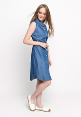 Beautiful cheerful young woman in a blue denim dress on a white background. Concept photo for clothing advertising. Isolate