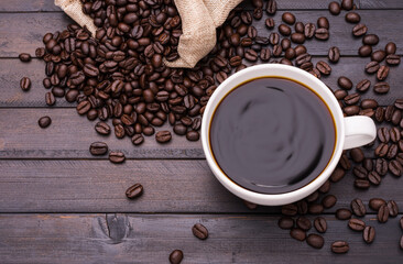 Dark coffee in a white coffee cup and roasted coffee beans placed on a black wooden table and there is space for text design.