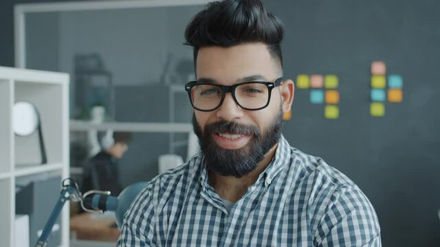 Portrait of attractive mixed race man wearing glasses smiling in modern workplace looking at camera. Businesspeople, emotions and job concept.