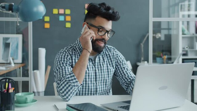 Slow Motion Of Young Middle Eastern Man Speaking On Mobile Phone In Office Sitting At Desk Talking And Gesturing. Communication And Job Concept.