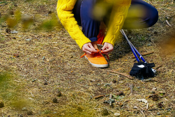 Sporty hiking woman tying shoelaces on her jogging shoes while taking a break after hiking in autumn forest. hiking concept, outdoor lifestyle.