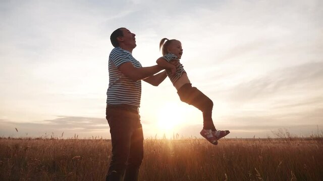 dad and daughter play in the park happy family. kid dream concept happy family playing. dad and daughter lifts her into the air fun play the pilot hands to the sides plane. happy family in the park