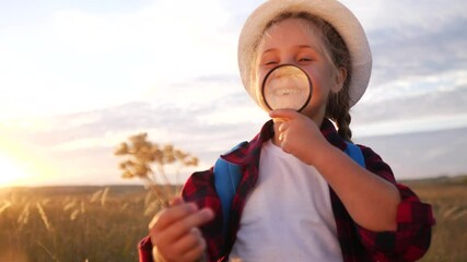 kid tourist examines the plant with a magnifying glass. travel tourism adventure concept. little kid boyscout girl with a backpack studies nature plant looks through a magnifying glass lifestyle