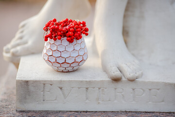 Red rowan berries in a vase near the feet of an antique statue. The inscription on the pedestal of...