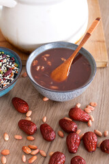 A bowl of prepared Laba porridge and a bowl of multi-grain ingredients on the table and jujube and peanuts scattered on the table