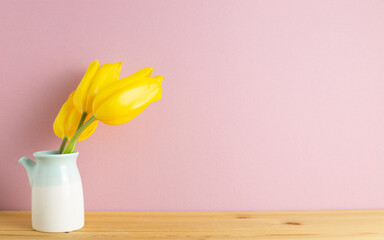 Yellow tulip flowers in vase on wooden table with pink background. copy space