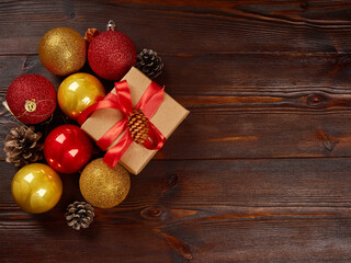 Christmas composition. Golden shiny balls, gift box with red ribbon, pine cones on a dark wooden background.