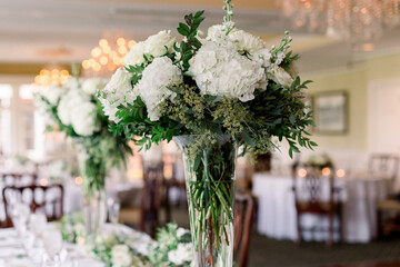 A gorgeous flower arrangement centerpiece with white flowers and green plants. This is the head table at a wedding reception. 