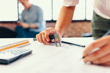 Engineering hands hold vernier caliper working and checking drawing blue print scale on workplace.