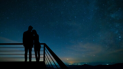 The romantic couple standing on the balcony on the scenic starry sky background