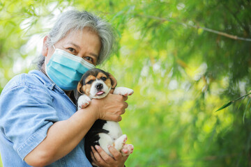 Portrait of Senior Asia woman with protective mask and with her puppy dog playing at the park.New normal style to protect virus.