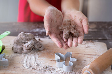Closeup of gingerbread biscuit dough shape for Christmas cookie, in child girl's hand, selective focus