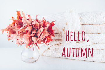 Fallen leaves in a vase with pile of white knitted Hello Autumn wording. Autumn, fall, beautiful nature , cozy home concept