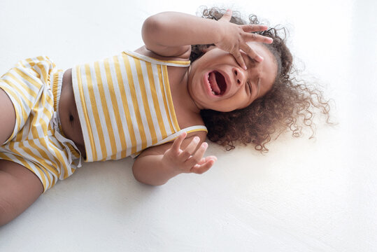 Dark skinned child girl crying and shouting with tantrum lying on the floor at home