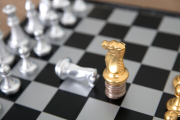 A silver horse chess piece on a chess board kneels to a golden horse chess piece standing on a coin