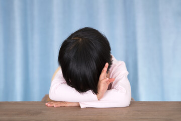 Little girl lying on the table in front of the blue curtain background pretending to sleep and refusing