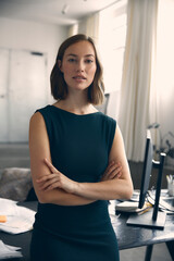 Young female entrepreneur standing in front of desk at the office, looking confident 