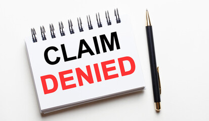 CLAIM DENIED written in a white notepad near a pen on a light background. Legal concept