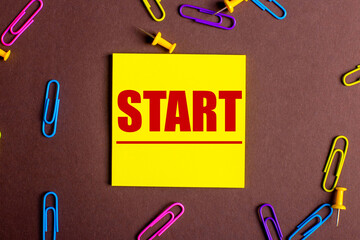 On a dark background, multi-colored paper clips and bright stickers with the word START