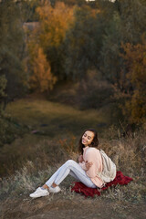 cute autumn girl in warm sweater enjoying nature in autumn forest, sitting on blanket with close eyes. Outdoor fall portrait.