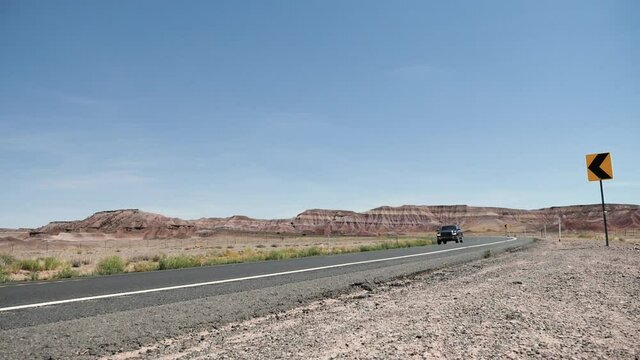 Pickup truck passing roadside camera in the countryside, blues sky, mountain range horizon, static shot