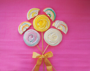 Bouquet of colored meringues on a stick with a bow on a pink background.
